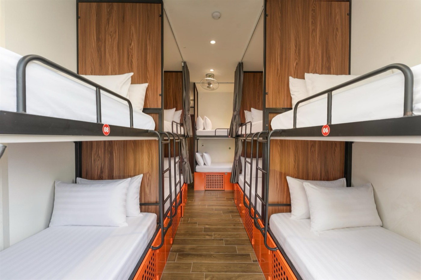 Dorm with two rows of steel bunks, curtains and orange lockers