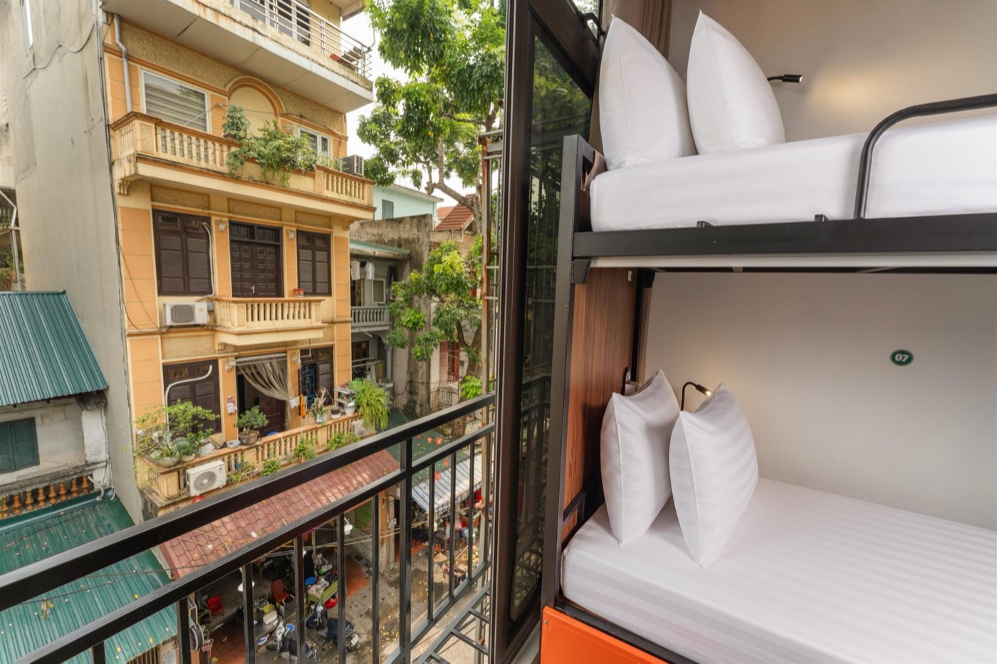 Bunk beside a window looking onto a yellow Hà Nội townhouse