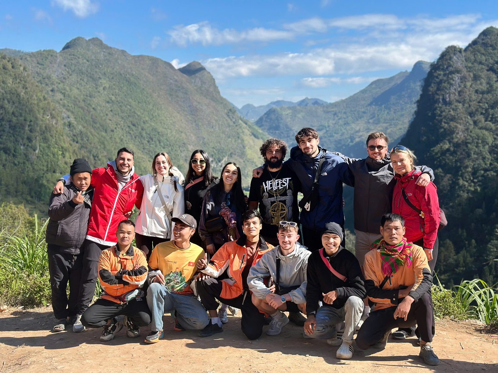 A big group of travellers and their easy-rider guides posing together at a viewpoint over a karst valley