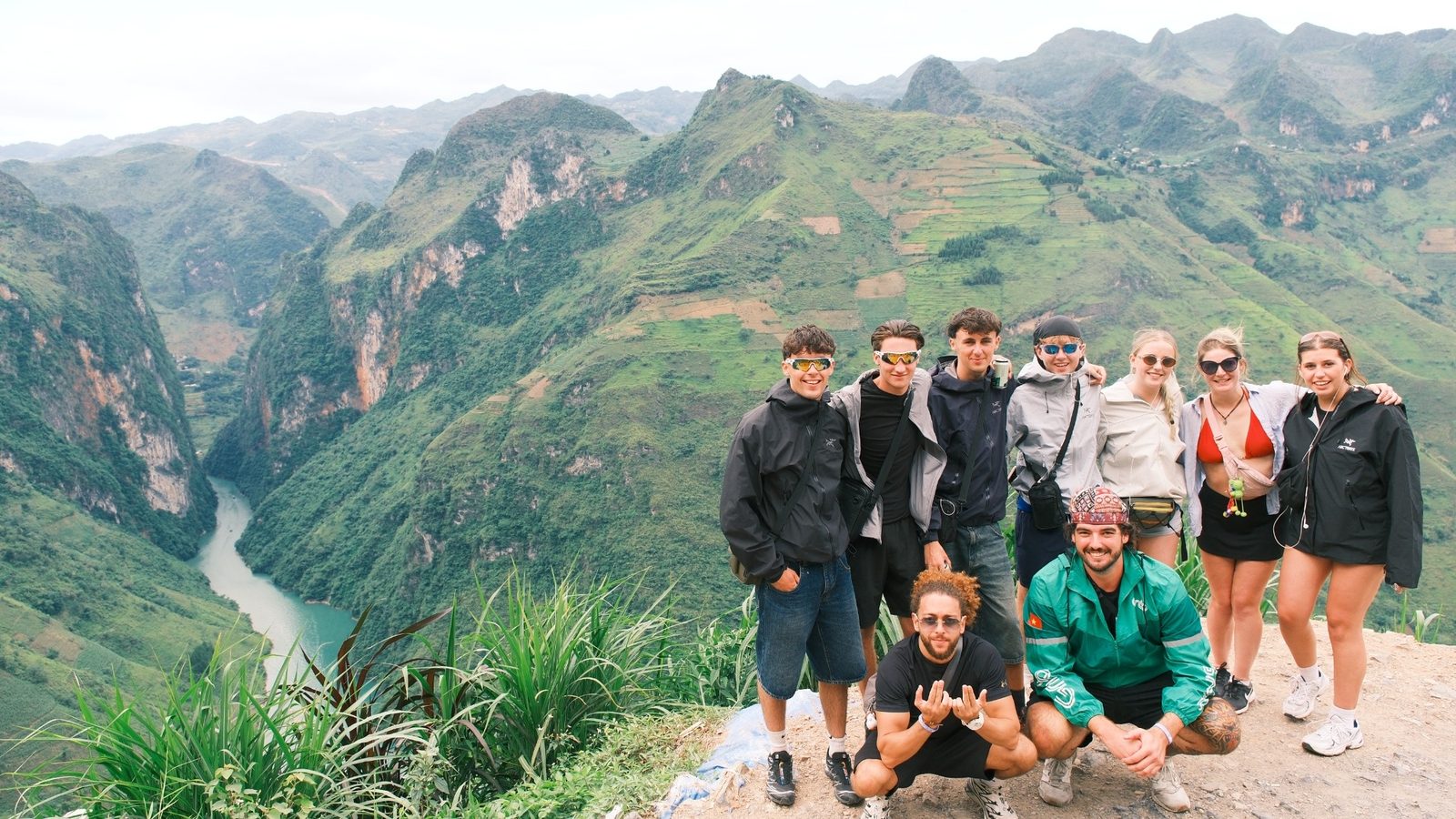 A group of travellers posing on a ledge high above the Nho Quế River canyon, karst peaks all around