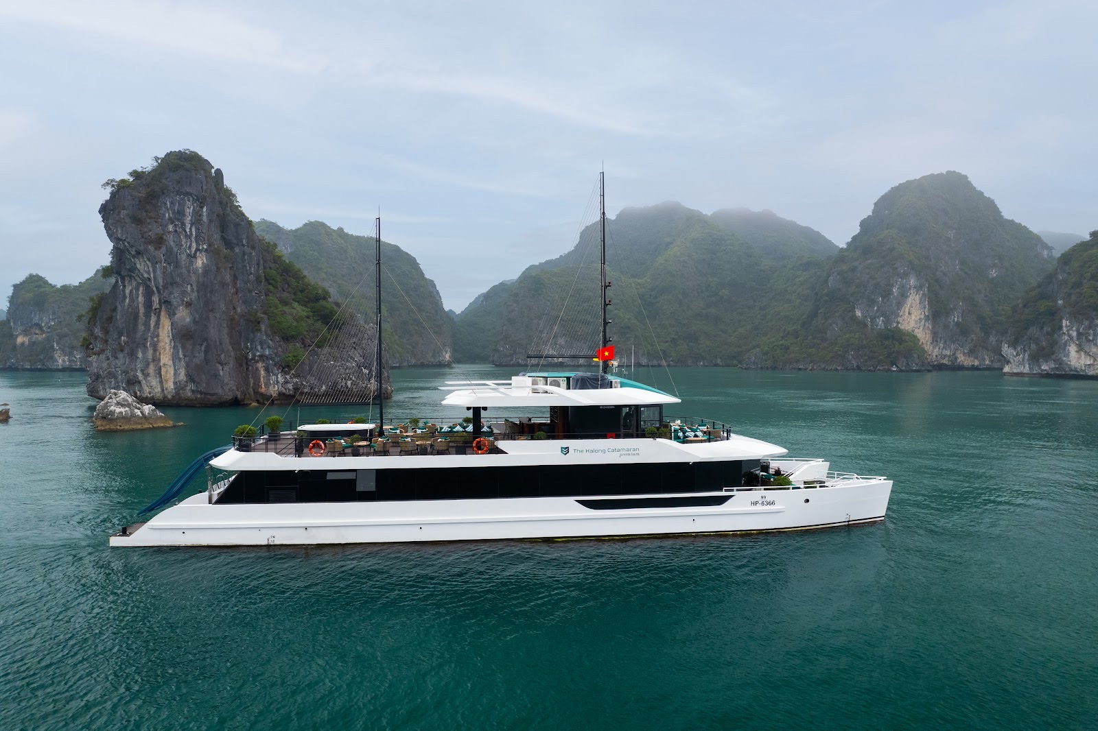 The white Halong Catamaran with its water slide at the stern, among misty limestone islands