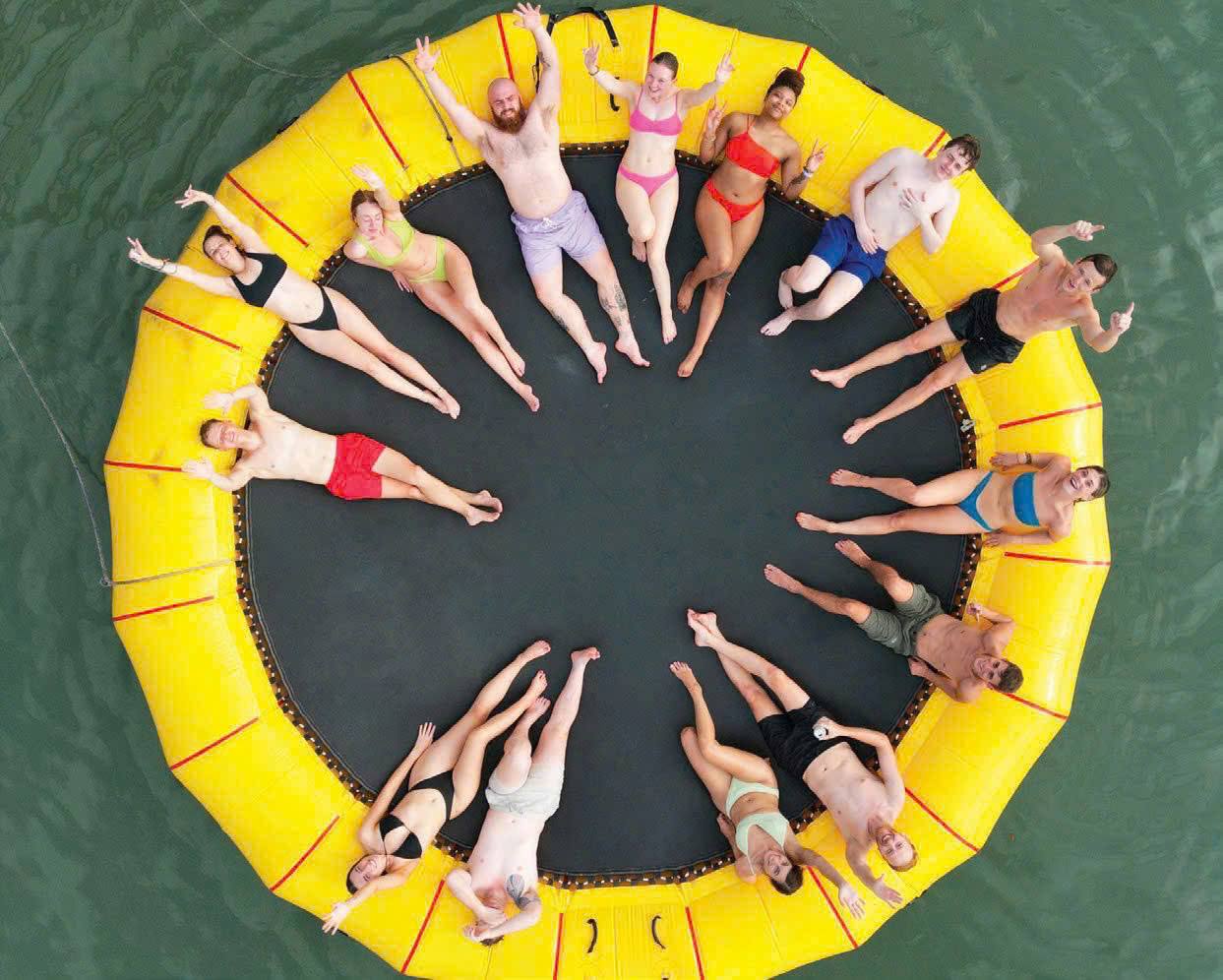 Aerial view of a group of guests lying in a circle on a yellow water trampoline