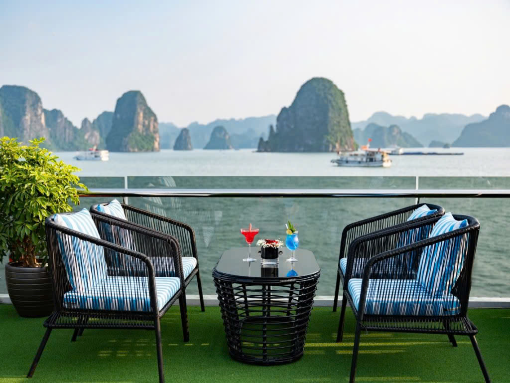 Two armchairs and a cocktail table at the sundeck rail, karst islands across Hạ Long Bay