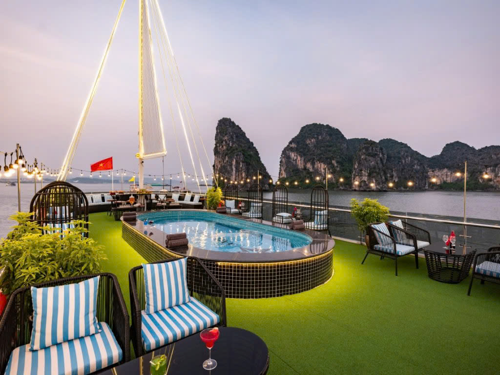 Striped loungers and a lit pool on the sundeck at dusk, karst islands behind
