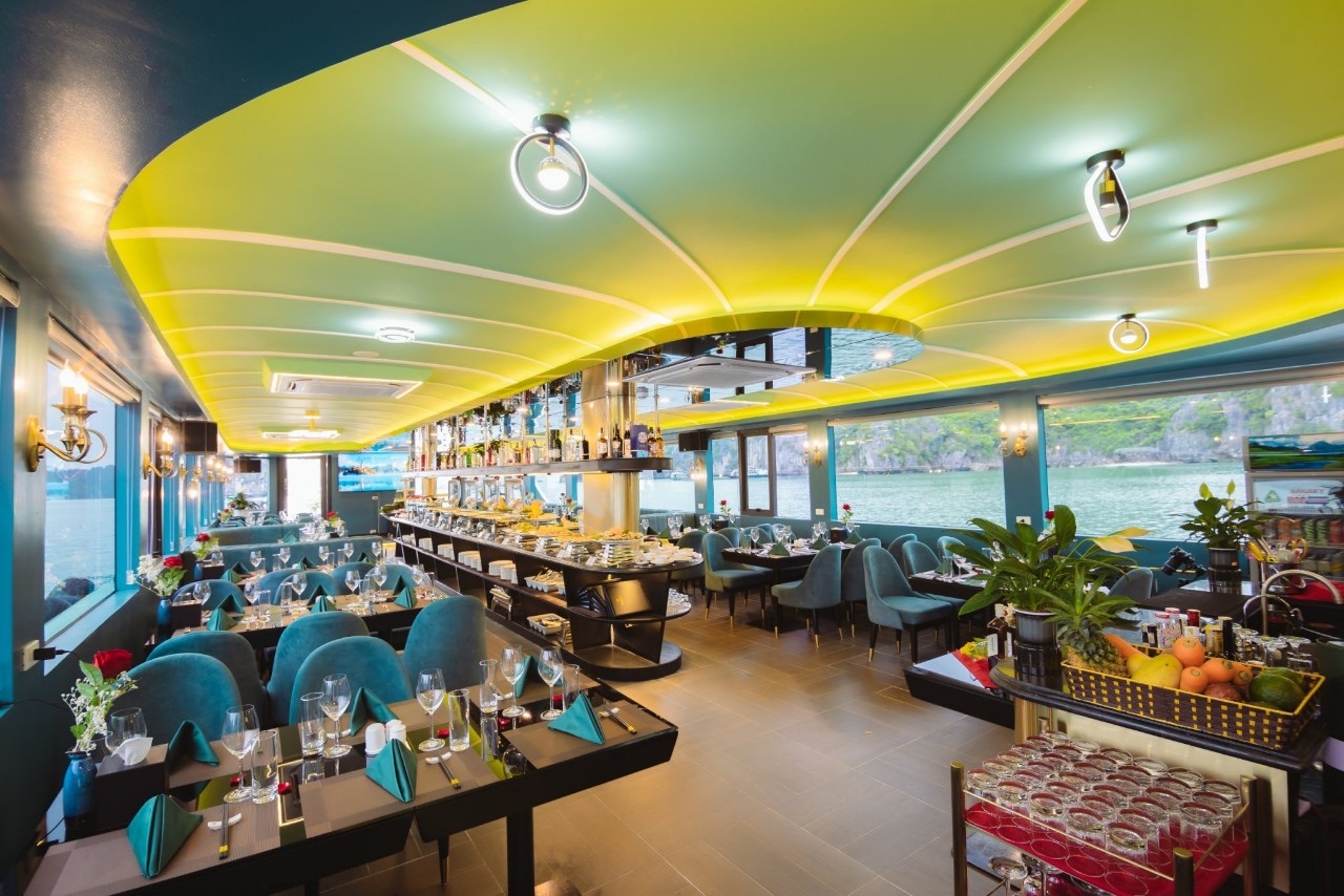 The boat’s dining room with teal chairs, a long buffet counter and bay views through the windows