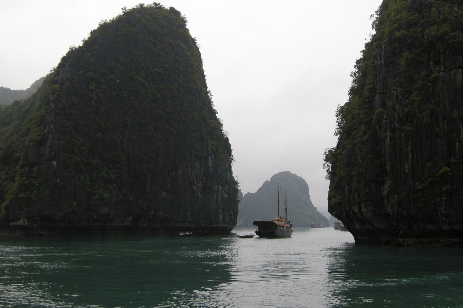 A small boat passing between tall karst towers in Hạ Long Bay