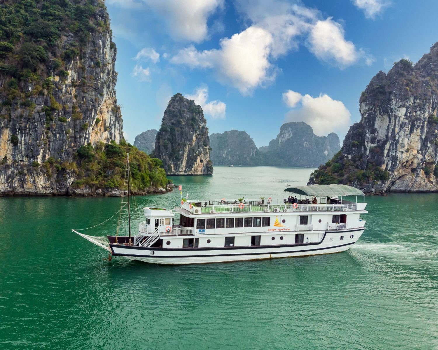 The white Sunlight Legend boat cruising between tall limestone islands in Hạ Long Bay
