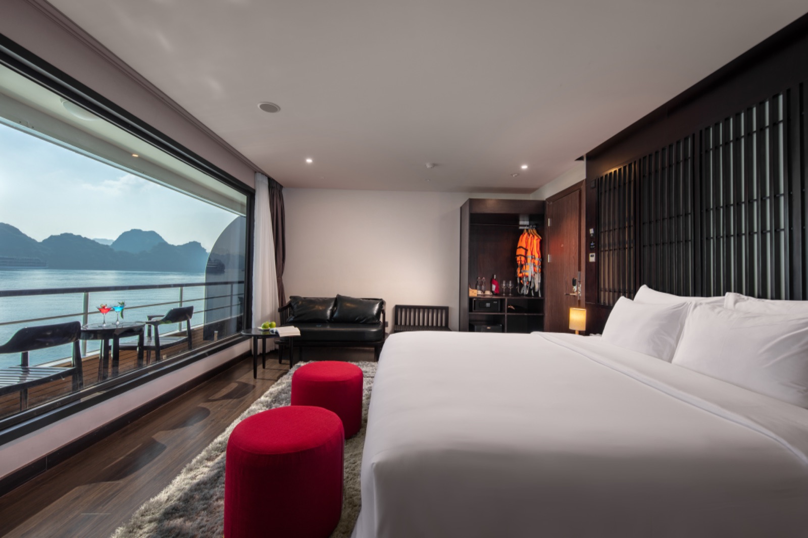 A cabin with a double bed, red footstools and a full-width window onto the bay