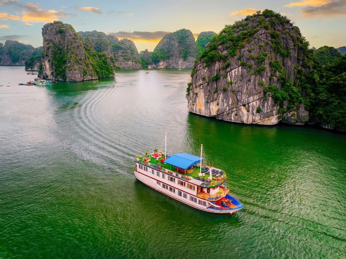 Aerial view of the Sunlight Premium boat sailing past limestone islands in Lan Hạ Bay at sunset