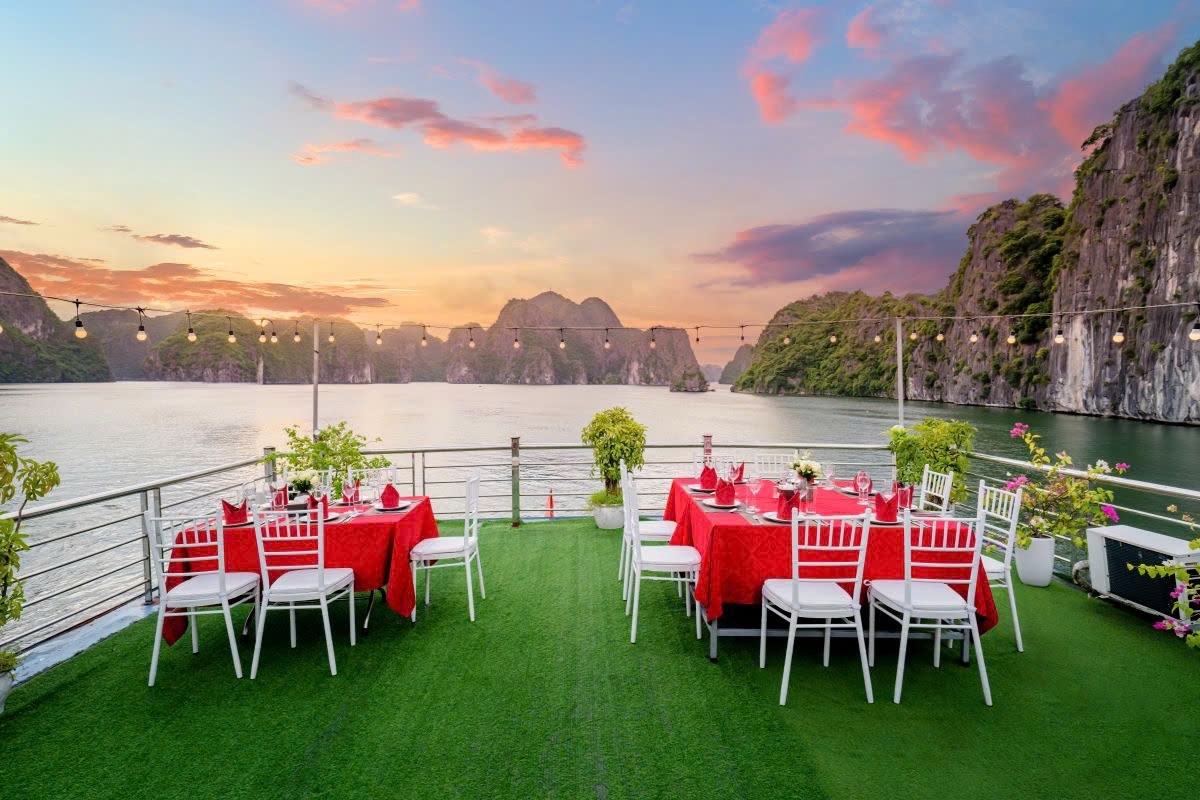 Tables laid with red cloths on the boat’s grass sundeck at sunset, karst cliffs behind