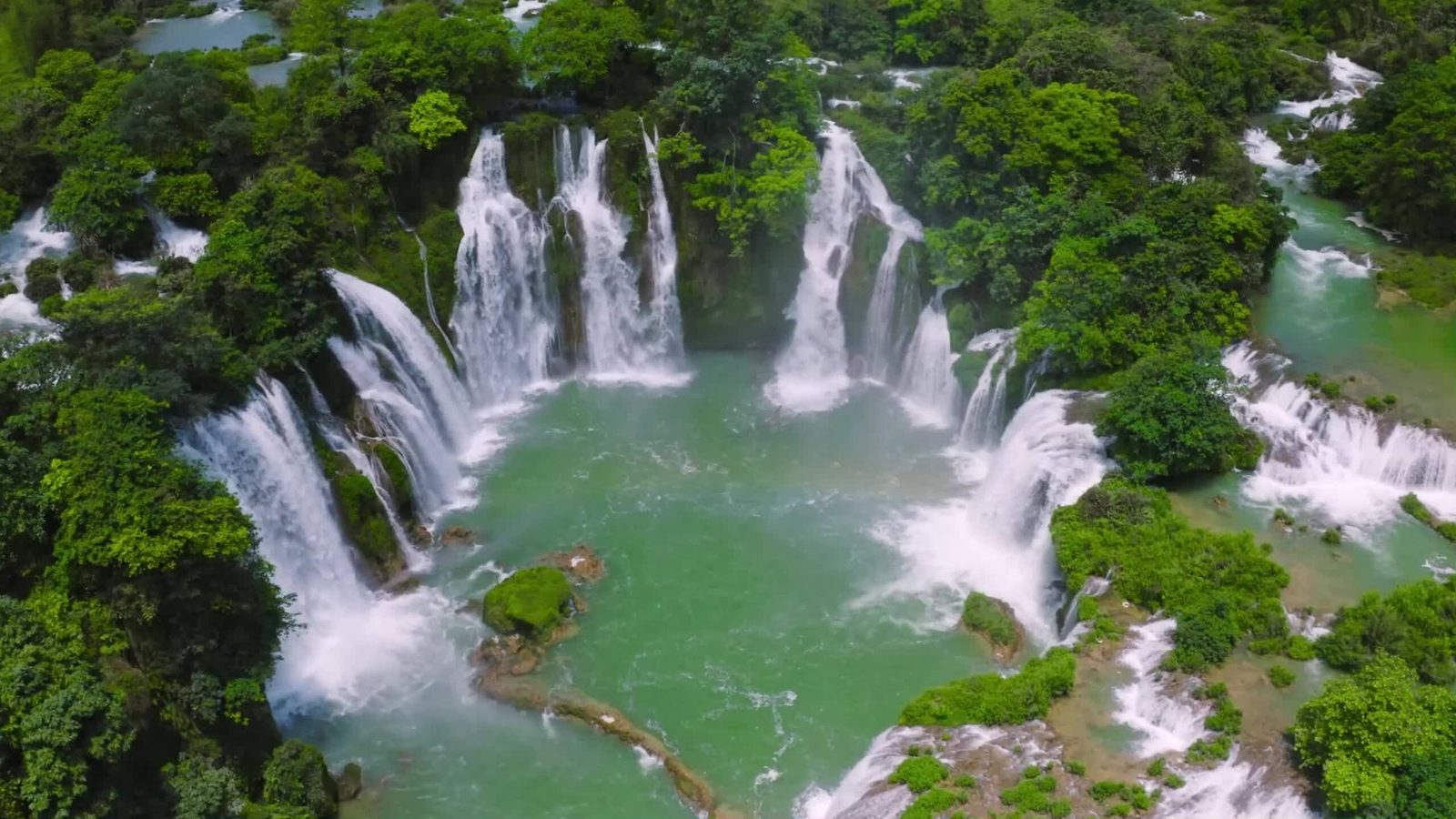 Bản Giốc waterfall from above: white cascades around a green pool in the forest
