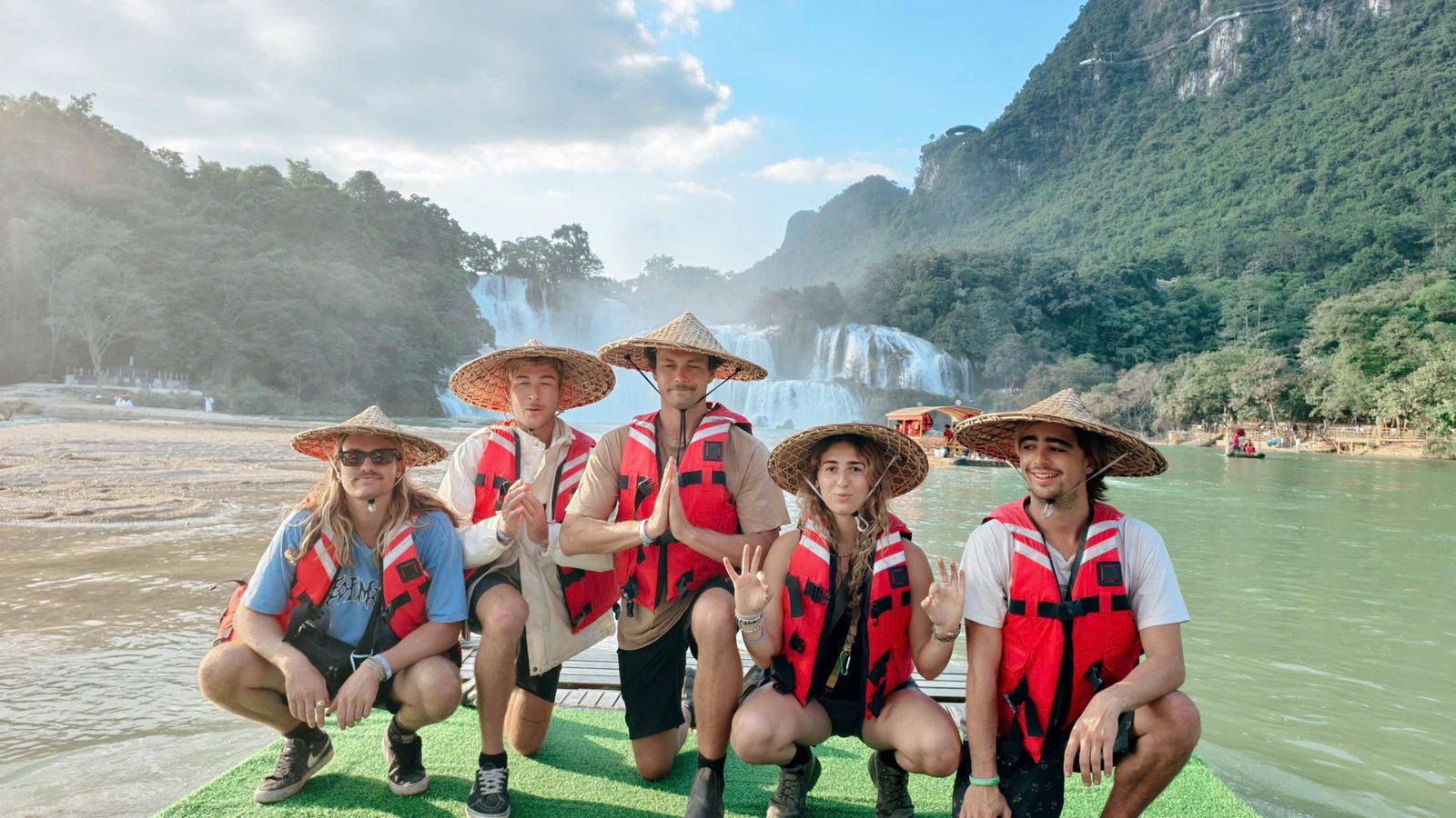 Five travellers in conical hats and life jackets on a raft below Bản Giốc waterfall
