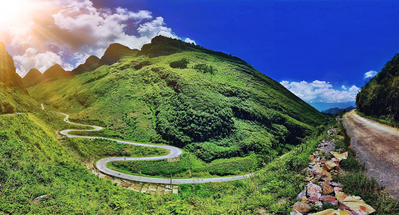A road snaking in hairpin bends across a green mountainside under a deep blue sky