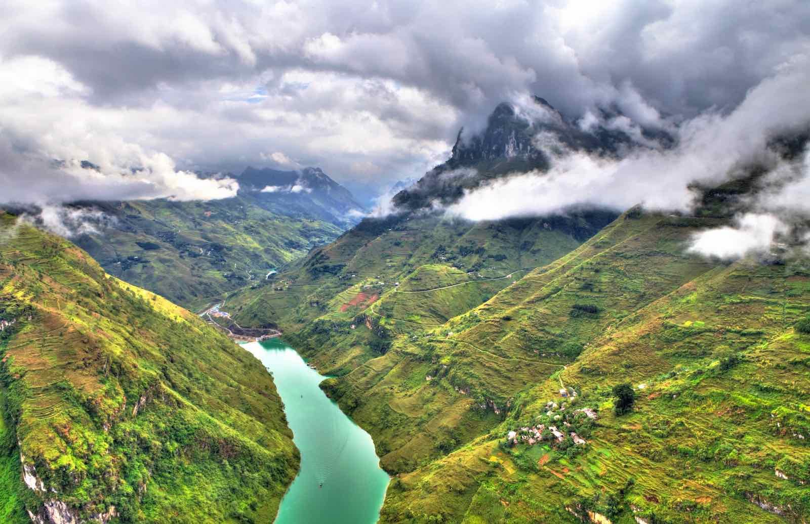 The turquoise Nho Quế River deep in a green canyon, clouds on the peaks above