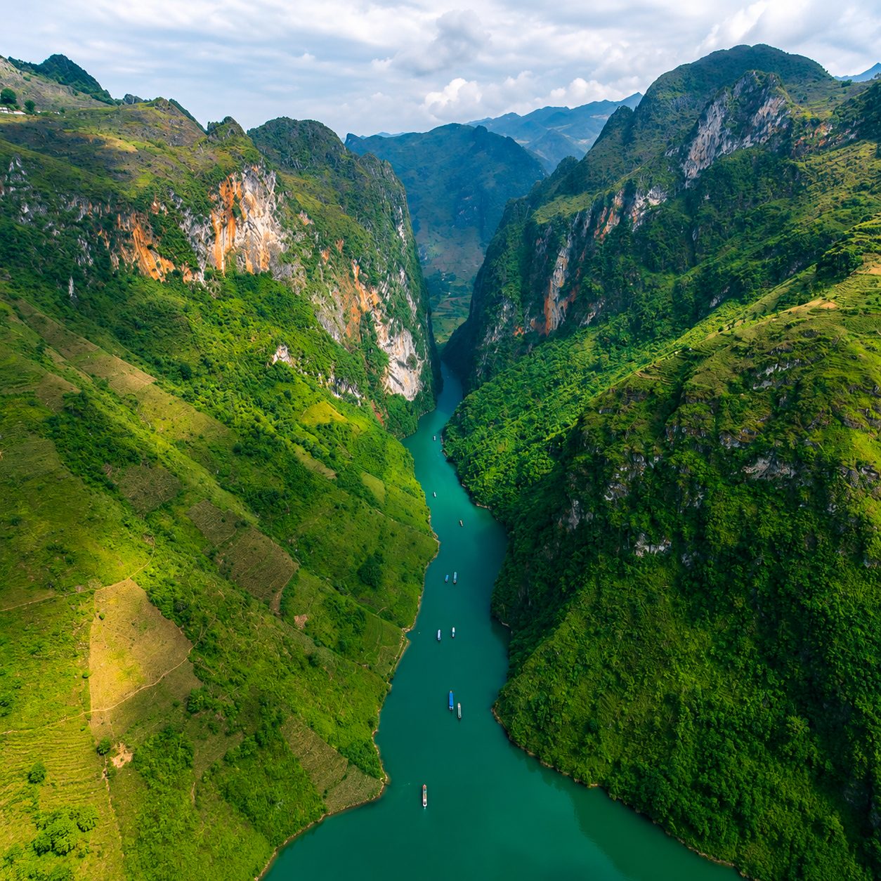 Small boats on the green Nho Quế river between steep canyon walls