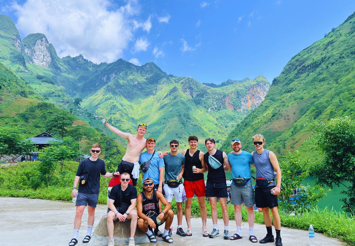 A group of friends posing by the road with green peaks and the river behind