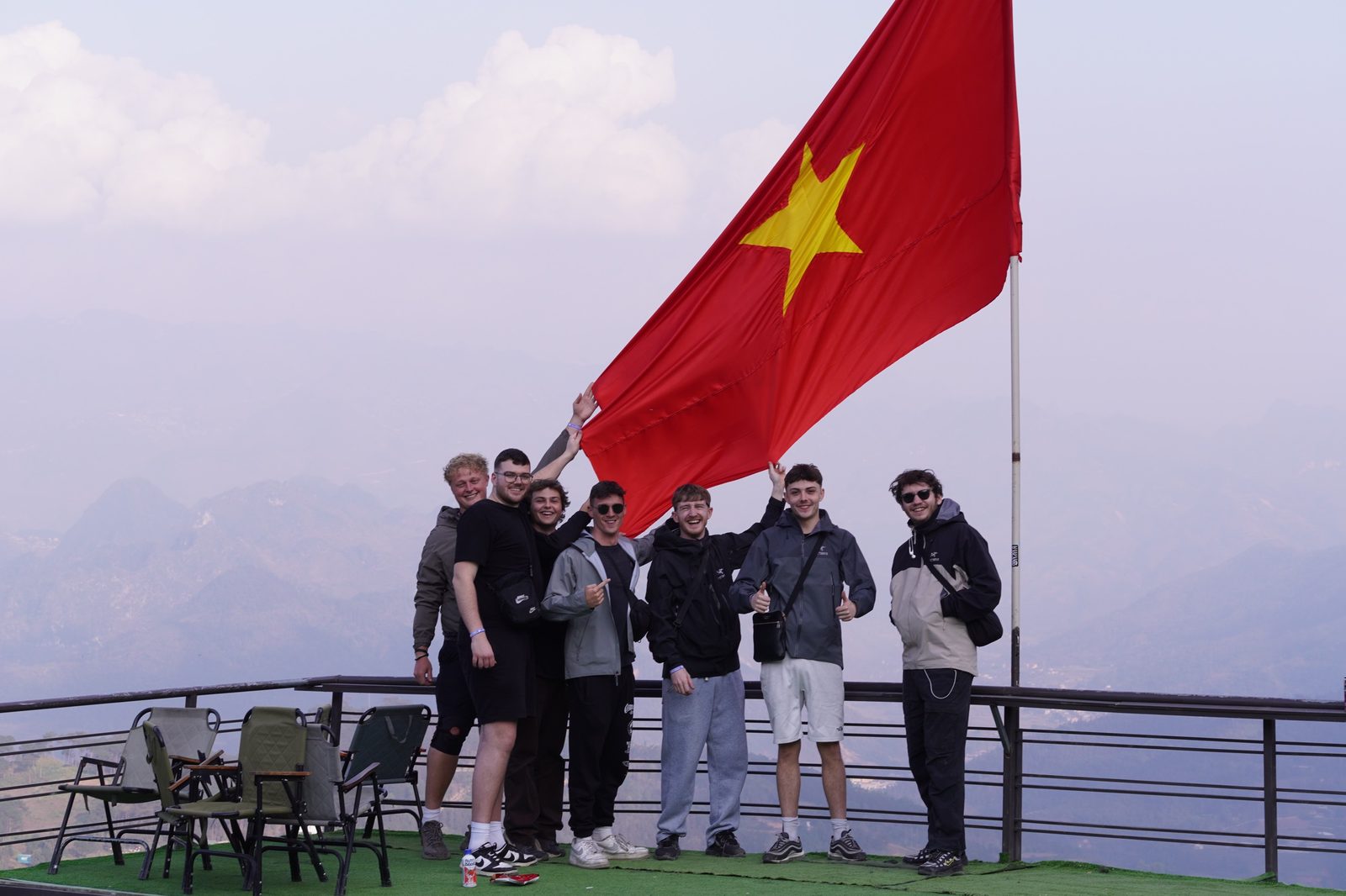 Young travellers holding up a big red flag on a misty mountain terrace