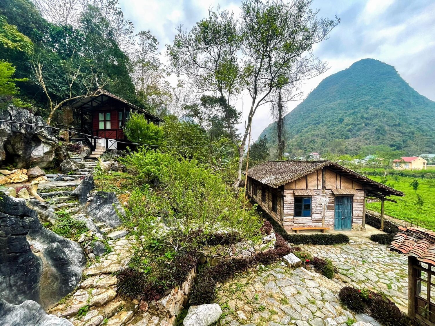 Wooden houses and a stone-paved yard among rocks, a green peak behind