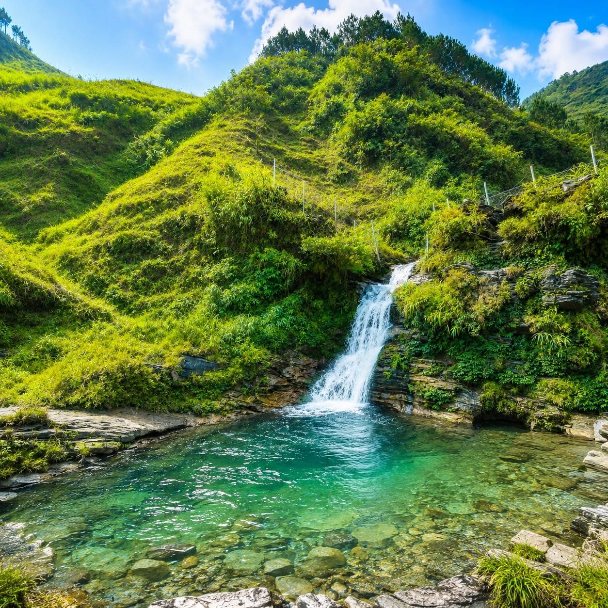 Du Già waterfall dropping into a clear green pool under grassy hills