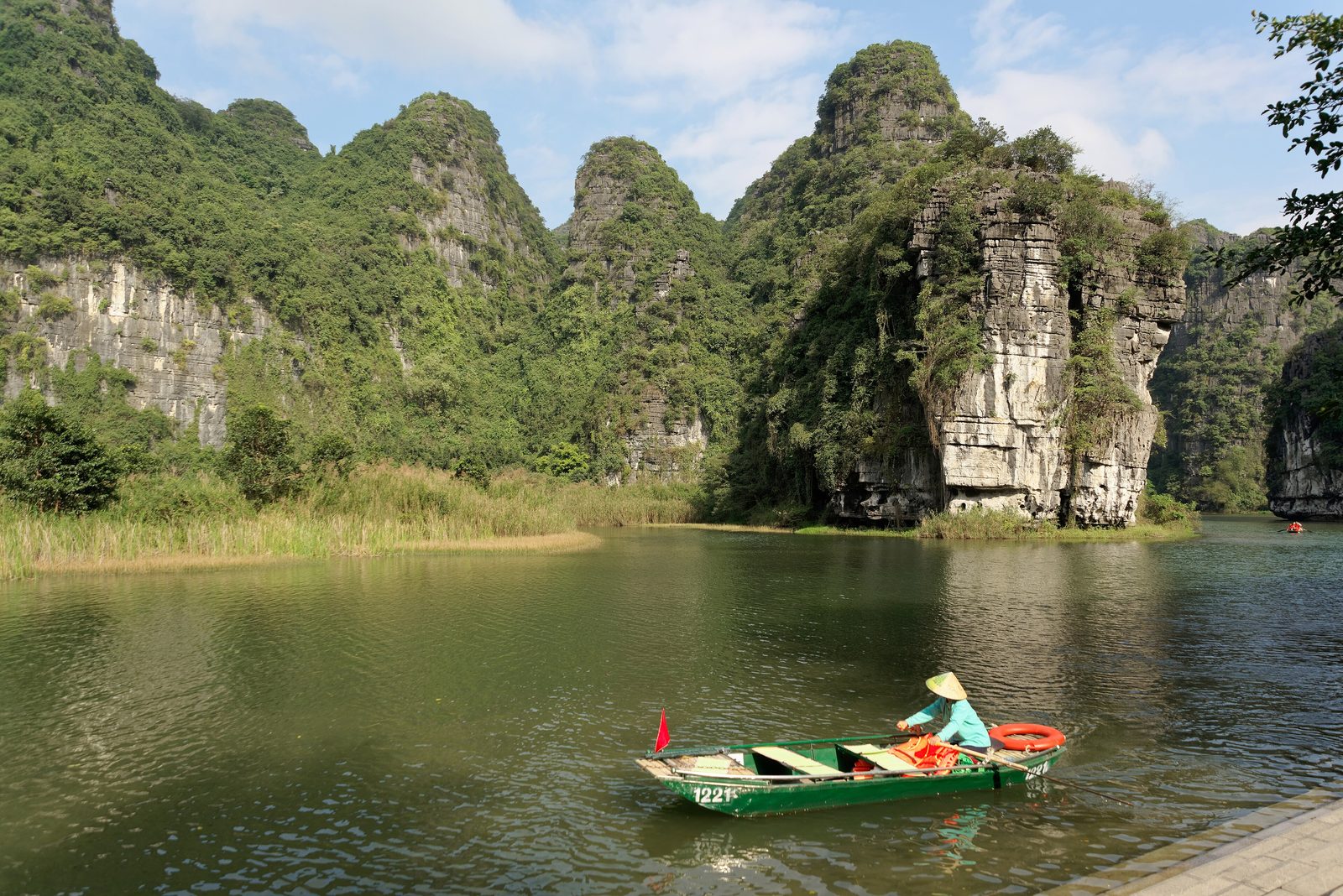A rower crossing a quiet lake ringed by cliffs in Tràng An